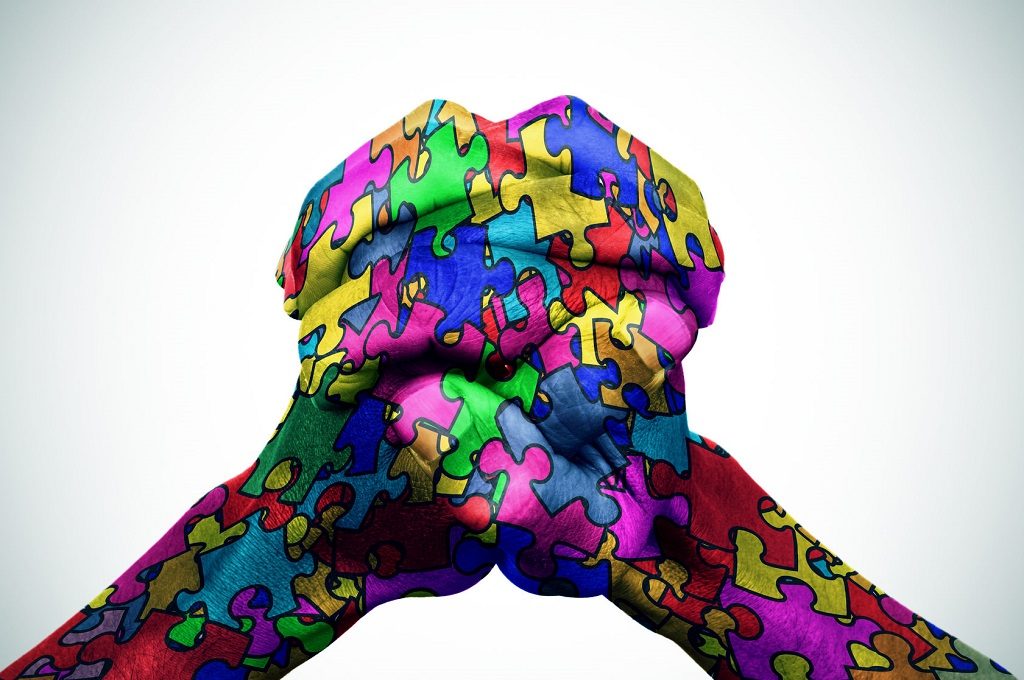 54039116 - man hands put together patterned with many puzzle pieces of different colors, symbol of the autism awareness, with a slight vignette added